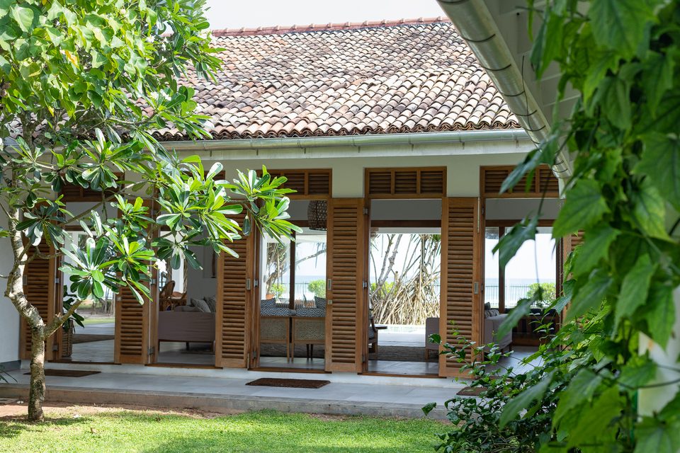The villa facade and open louvred shutters seen through frangipani
