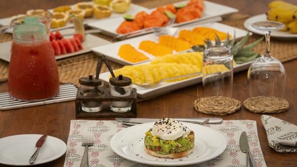 Breakfast laid out on the villa’s dining table — tropical fruit, fresh juice and avocado on toast